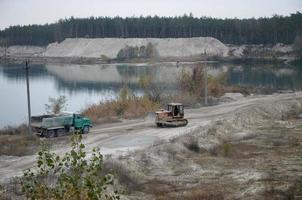 Caterpillar loader and dump truck works at the opencast mining quarry. Heavy machinery in the open pit at river. Dozer and truck on digging operations photo