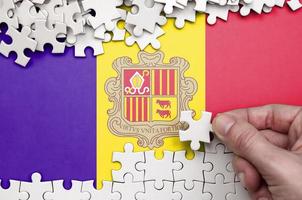 Andorra flag  is depicted on a table on which the human hand folds a puzzle of white color photo