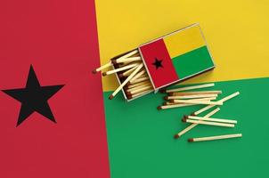 Guinea Bissau flag  is shown on an open matchbox, from which several matches fall and lies on a large flag photo