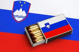 Slovenia flag  is shown in an open matchbox, which is filled with matches and lies on a large flag photo