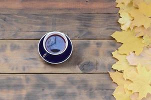 una taza de té entre un conjunto de hojas de otoño caídas amarillentas sobre una superficie de fondo de tablas de madera natural de color marrón oscuro foto