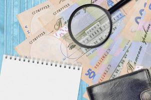 500 Ukrainian hryvnias bills and magnifying glass with black purse and notepad. Concept of counterfeit money. Search for differences in details on money bills to detect fake photo