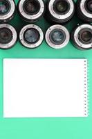 Several photographic lenses and white notebook lie on a bright turquoise background. Copy space photo