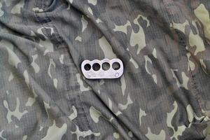 Iron brass cnuckles on crumpled camouflage clothes close up. Football hooliganism and racism concept photo