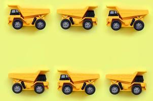 Many small yellow toy trucks on texture background of fashion pastel yellow color paper in minimal concept photo
