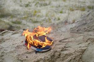 Burning sports sneakers or gym shoes on fire stand on sandy beach coast. Athlete burned out. Physical exertion during training concept photo