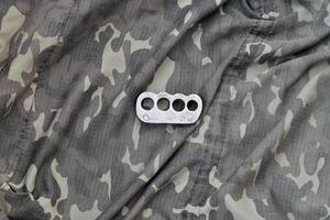 Iron brass cnuckles on crumpled camouflage clothes close up. Football hooliganism and racism concept photo