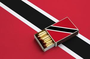 Trinidad and Tobago flag  is shown in an open matchbox, which is filled with matches and lies on a large flag photo