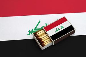 Iraq flag  is shown in an open matchbox, which is filled with matches and lies on a large flag photo