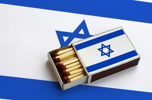 Israel flag  is shown in an open matchbox, which is filled with matches and lies on a large flag photo