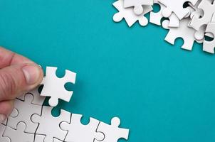 The hand folds a white jigsaw puzzle and a pile of uncombed puzzle pieces lies against the background of the blue surface. Texture photo with space for text