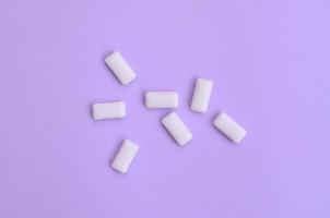 unos cuantos chicles se encuentran en el fondo de textura del papel de color violeta pastel de moda en un concepto mínimo foto