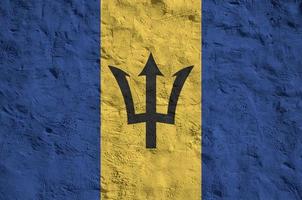 Barbados flag depicted in bright paint colors on old relief plastering wall. Textured banner on rough background photo