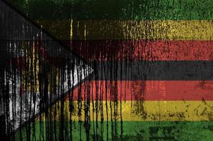 Zimbabwe flag depicted in paint colors on old and dirty oil barrel wall closeup. Textured banner on rough background photo