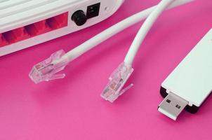 el enrutador de Internet, el adaptador wi-fi usb portátil y los enchufes de cable de Internet se encuentran sobre un fondo rosa brillante. elementos necesarios para internet foto