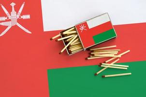 Oman flag  is shown on an open matchbox, from which several matches fall and lies on a large flag photo