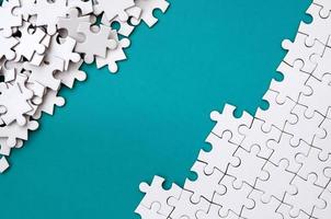 Fragment of a folded white jigsaw puzzle and a pile of uncombed puzzle elements against the background of a blue surface. Texture photo with space for text