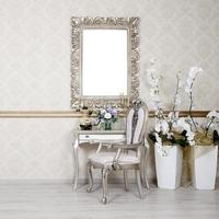 A fragment of a retro interior with a chair and table, on which is a telephone and a vase of flowers. Above the table hangs an empty picture frame for your photo