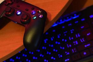 el gamepad moderno se encuentra con el teclado de la pc en la mesa en la escena oscura de la sala de juegos. concepto cooperativo de juego en equipo foto