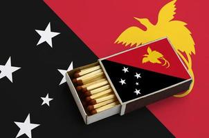 Papua New Guinea flag  is shown in an open matchbox, which is filled with matches and lies on a large flag photo