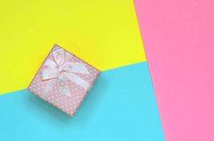una pequeña caja de regalo rosa se encuentra en el fondo de textura de papel de colores azul pastel, amarillo y rosa de moda en un concepto mínimo foto