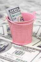 A bundle of US dollars in a metal pink bucket on a set of dollar bills photo