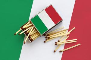 Italy flag  is shown on an open matchbox, from which several matches fall and lies on a large flag photo