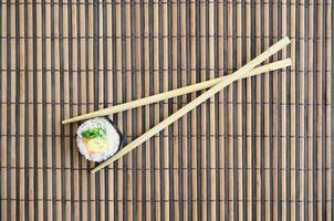 Sushi roll and wooden chopsticks lie on a bamboo straw serwing mat. Traditional Asian food. Top view. Flat lay minimalism shot with copy space photo