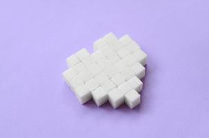 A heart made of sugar cubes lies on a trendy pastel violet background photo