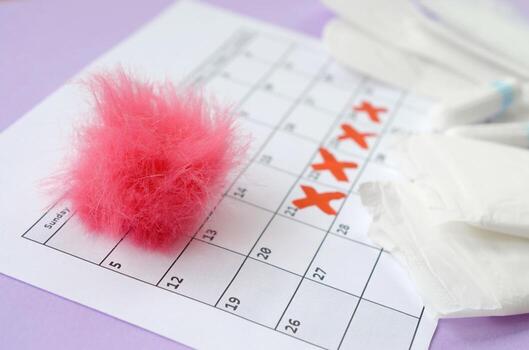 Menstrual pads and tampons on menstruation period calendar with red cross marks lies on lilac background photo