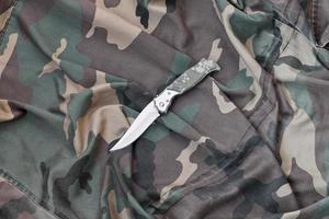 Military knife on army camouflage clothes close up. Background with copy space for military or special service design photo