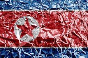 North Korea flag depicted in paint colors on shiny crumpled aluminium foil closeup. Textured banner on rough background photo