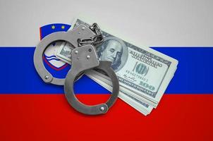 Slovenia flag  with handcuffs and a bundle of dollars. Currency corruption in the country. Financial crimes photo
