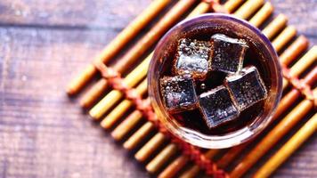 A glass of soda with ice on a bamboo coaster, top view video