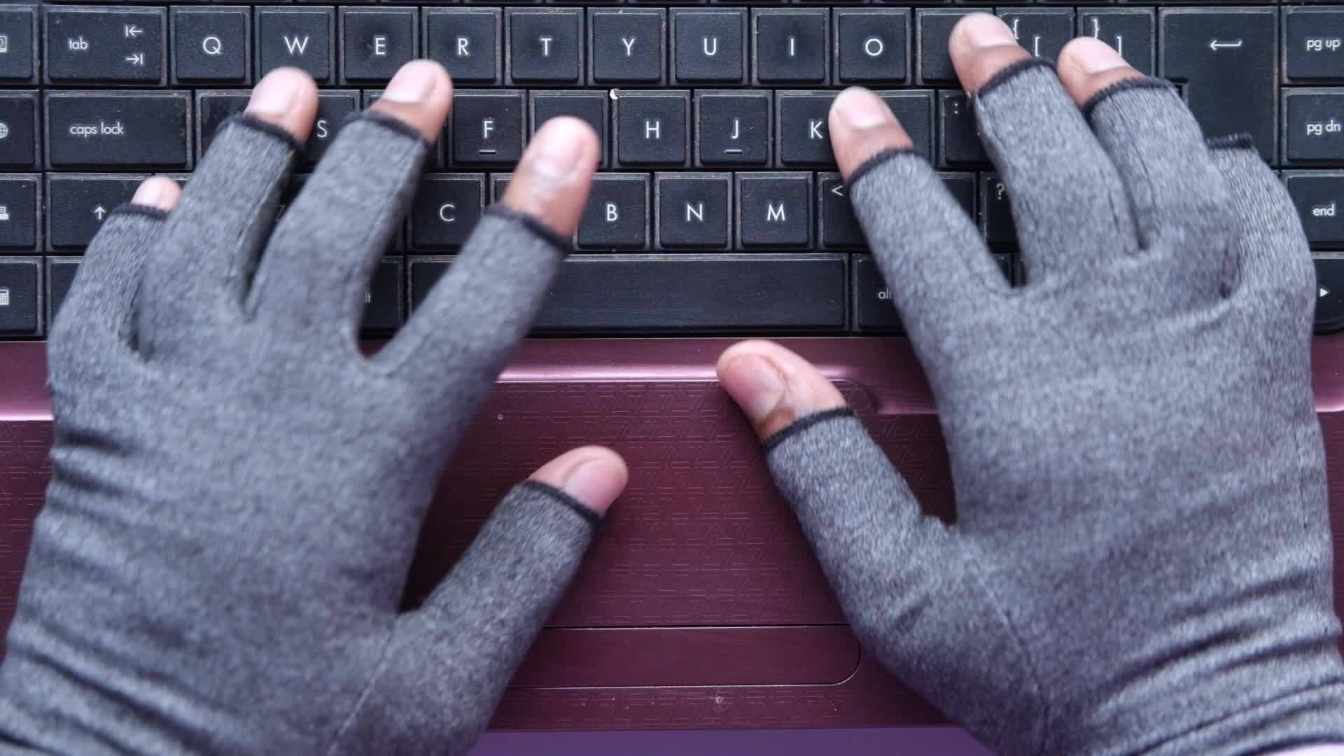 Person with fingerless gloves types on computer keyboard