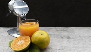 jugo de naranja en vidrio y cítricos frescos alrededor con exprimidor manual de frutas en la mesa de madera. copie el espacio foto