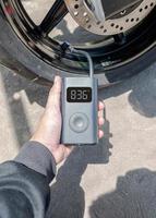 Hand holding a portable inflator is inflating a motorcycle tire. photo