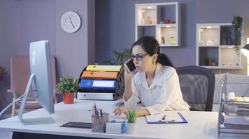 mujer de negocios hablando por teléfono y mirando la computadora. empresaria hablando por teléfono por la noche en su oficina en casa. video