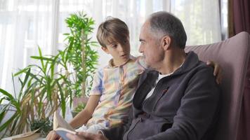 ben informato nonno e intelligente nipote lettura un' libro. nonno legge un' libro per il suo nipote e il nipote ascolta con attenzione. video