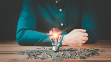 A glowing light bulb on pile money cions on a wooden table, business problem solving ideas and creative marketing ideas Inventing, save money and learning new things. photo