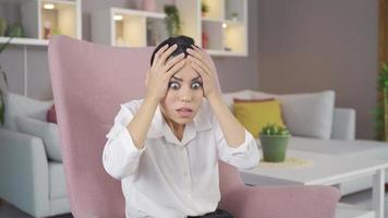 Frightened woman panics. The young woman sitting in the berjer at home is in fear and panic. video