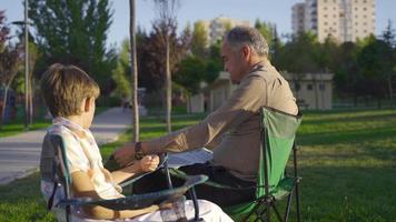el abuelo está charlando con su nieto al aire libre. anciano leyendo el periódico al aire libre. video