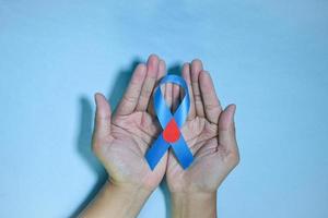 Top View Blue ribbon awareness with red blood drop in man hands isolated on a blue background. 14 november, World diabetes day. Copyspace photo