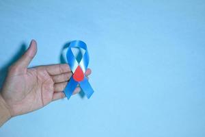 vista superior conciencia de la cinta azul con gota de sangre roja en las manos del hombre aislado en un fondo azul. 14 de noviembre, día mundial de la diabetes. espacio de copia foto