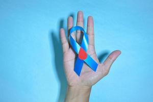 Top View Blue ribbon awareness with red blood drop in man hands isolated on a blue background. 14 november, World diabetes day. Copyspace photo