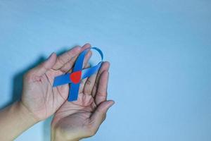 Top View Blue ribbon awareness with red blood drop in man hands isolated on a blue background. 14 november, World diabetes day. Copyspace photo