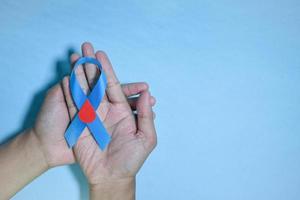 Top View Blue ribbon awareness with red blood drop in man hands isolated on a blue background. 14 november, World diabetes day. Copyspace photo