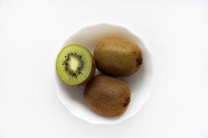 kiwi fresco y jugoso, picado y entero en un plato blanco. deliciosas frutas y trozos de kiwi verde. foto