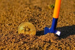 Bitcoin coin and shovel in sand at sunset.Digital currency mining.