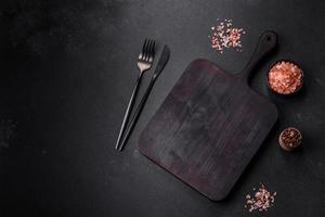Wooden cutting board with kitchen appliances on a black concrete background photo